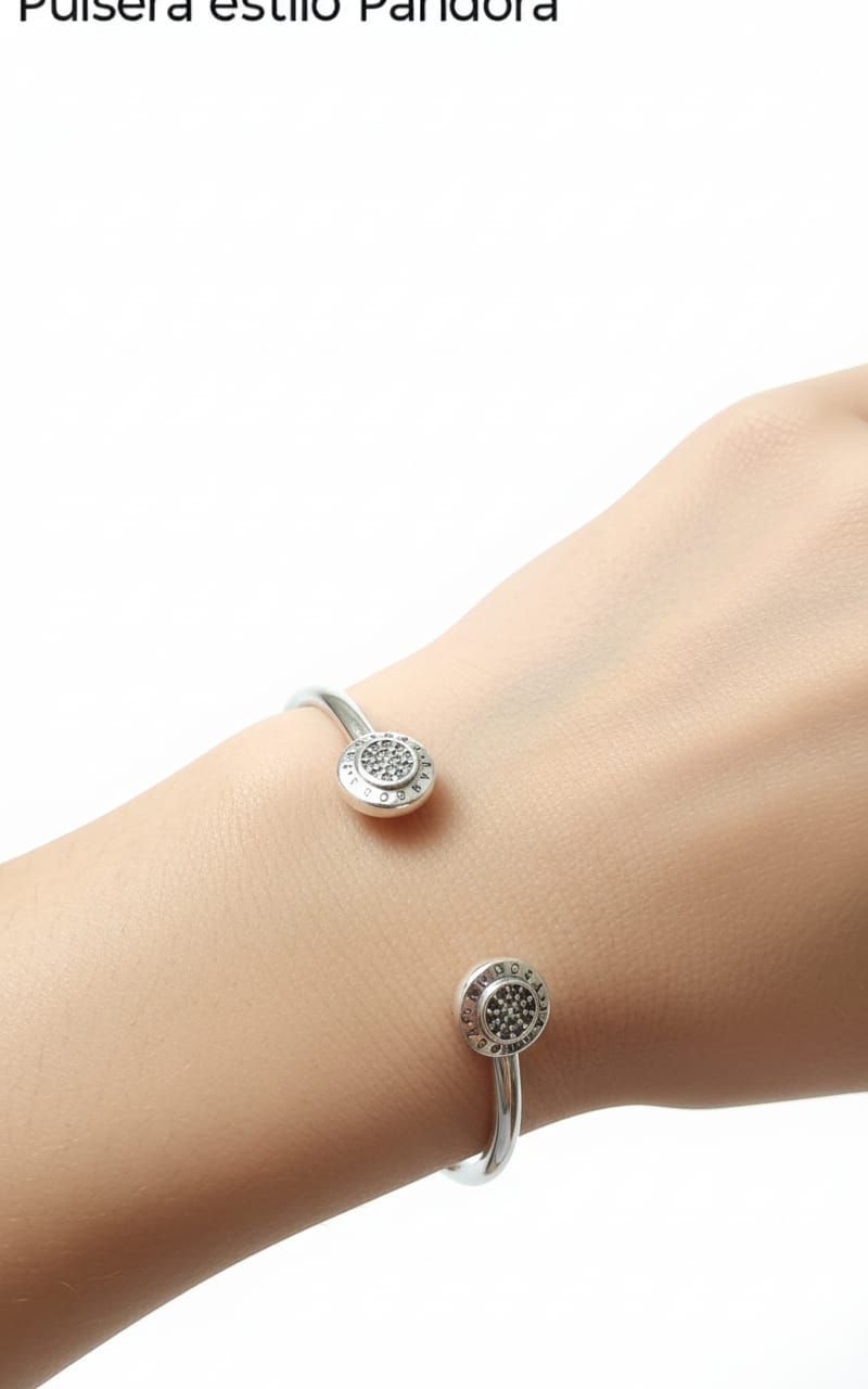 Dos pulseras Pandora de plata con dijes en una muñeca de piel clara, mostradas sobre un fondo blanco.