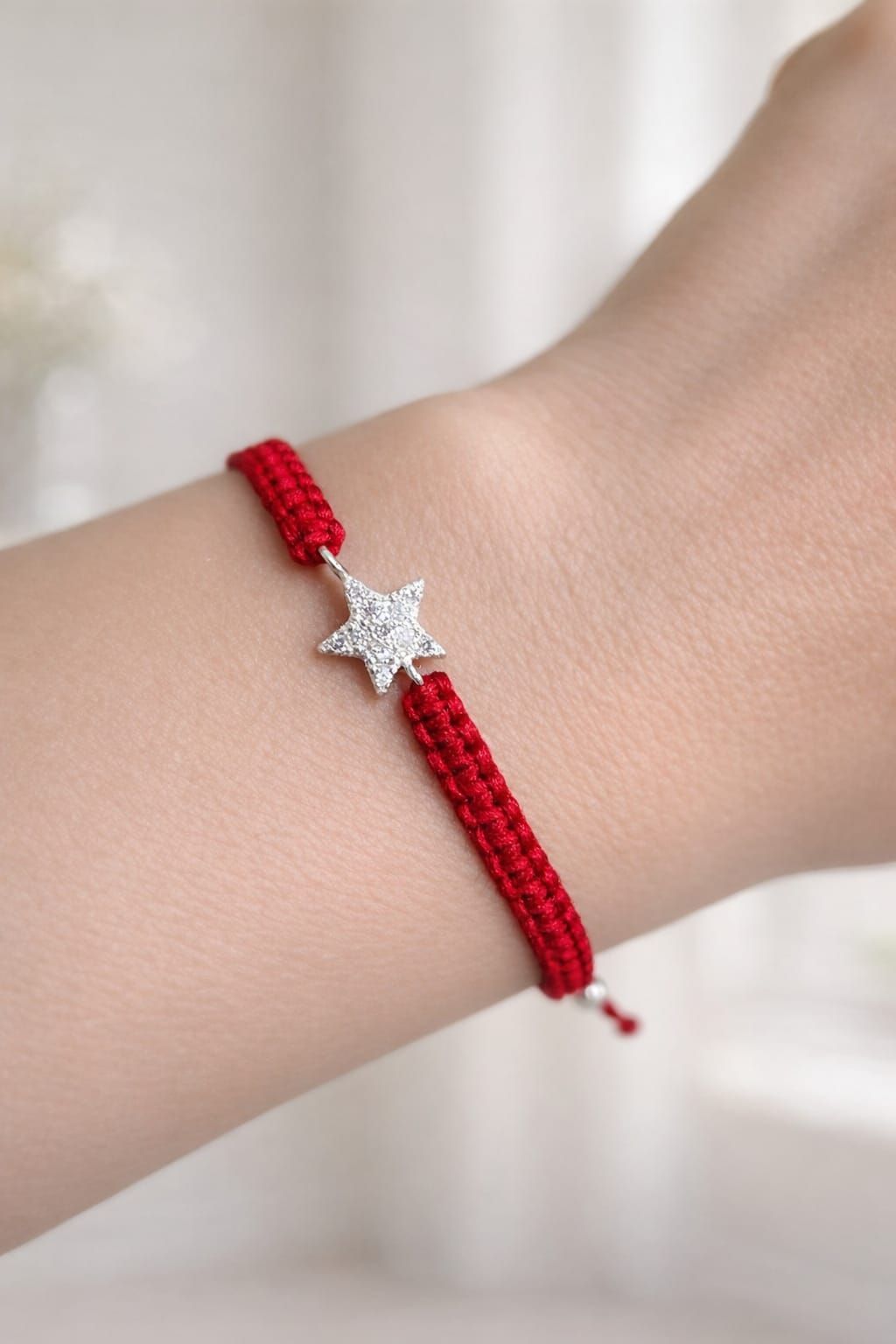 Pulsera trenzada roja con un dije de estrella plateada en la muñeca.