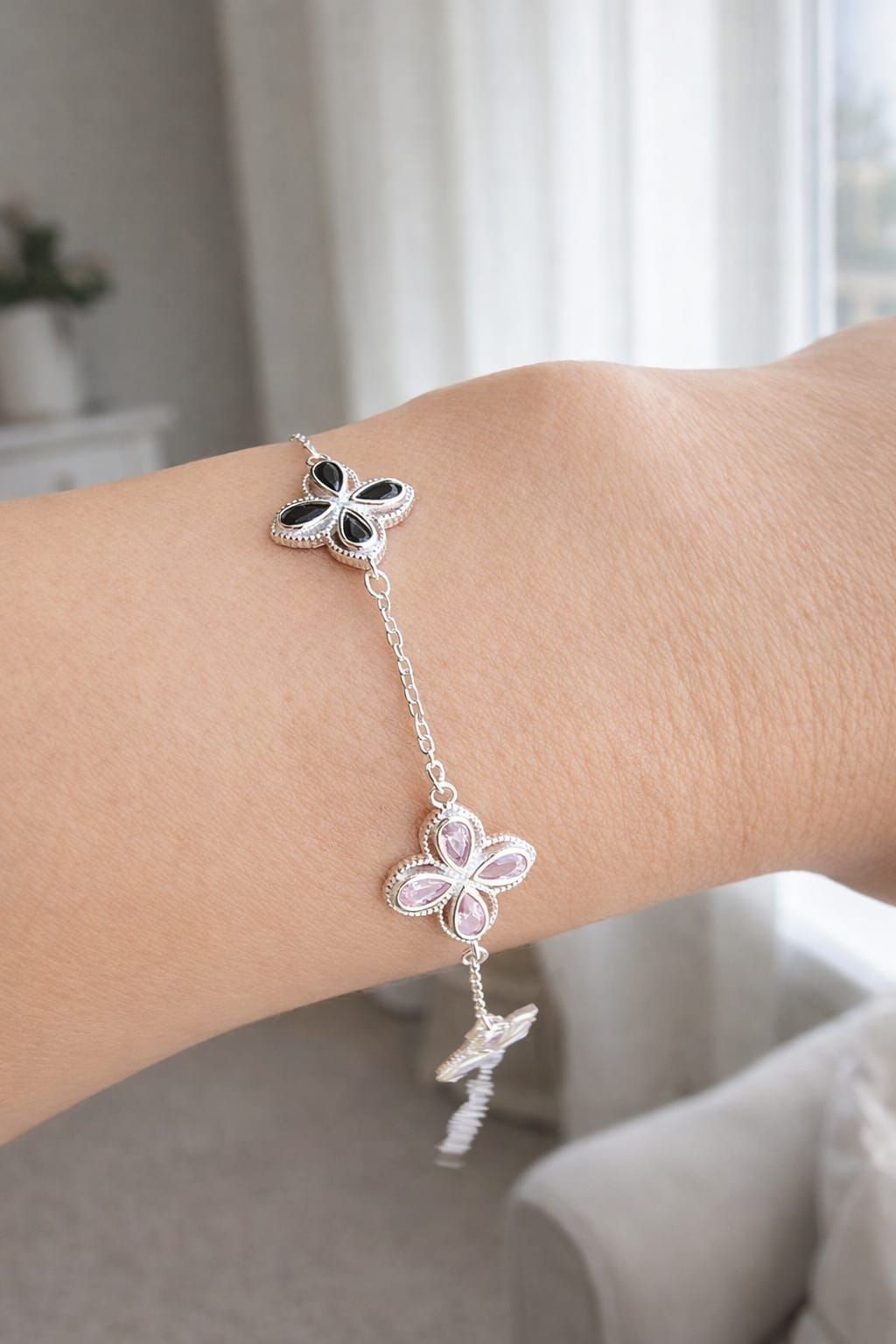 Pulsera con dije de mariposa plateada en la muñeca, con detalles en rosa y negro.