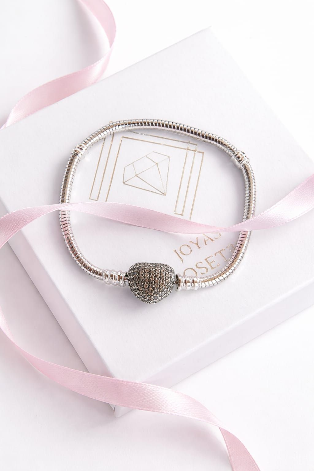Mujer abrochándose una pulsera de plata en la muñeca, vestida con una blusa blanca sin mangas.