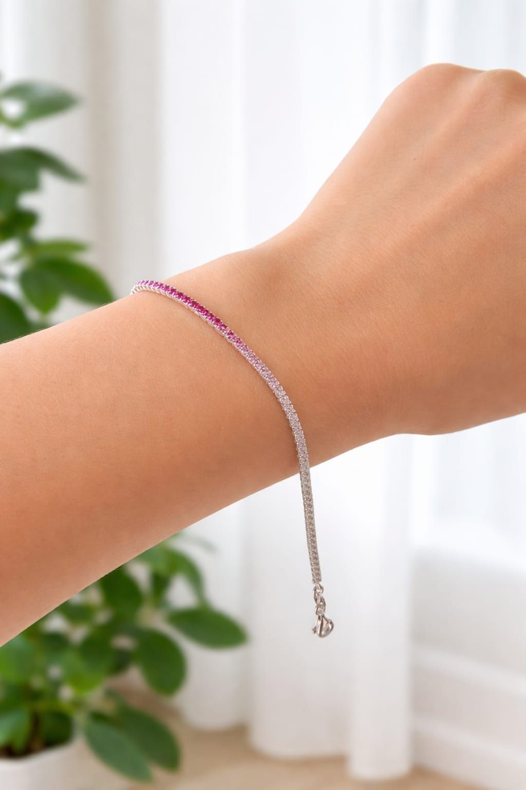 Mano que lleva una pulsera de cuentas rosas y plateadas con un colgante de cadena.