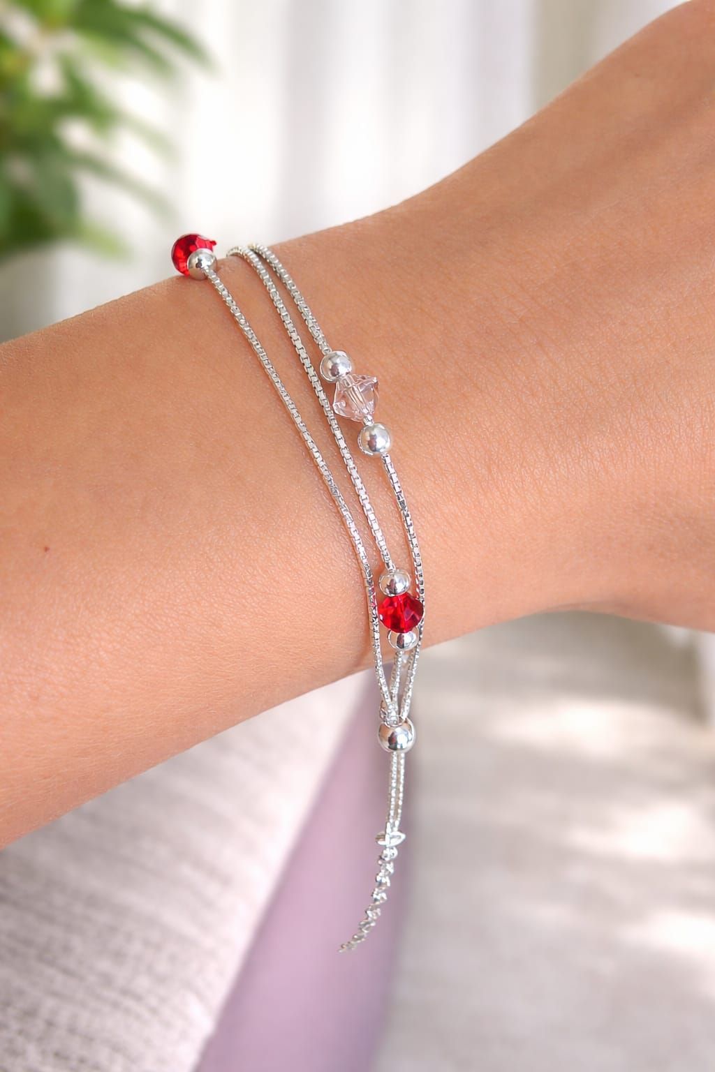 Pulsera de cuentas plateadas con detalles rojos en una muñeca, primer plano sobre un fondo suave.