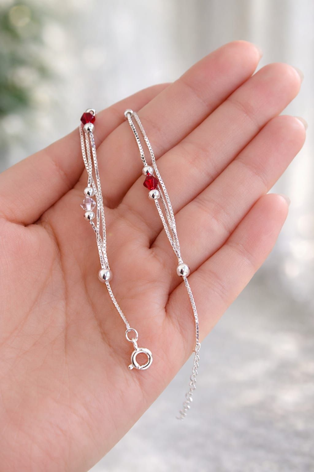 Pulsera de cuentas plateadas con detalles rojos en una muñeca, primer plano sobre un fondo suave.