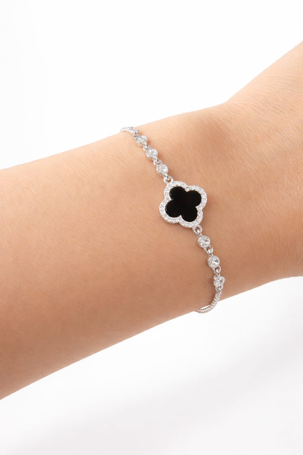 Pulsera de plata con un dije de trébol negro en la muñeca