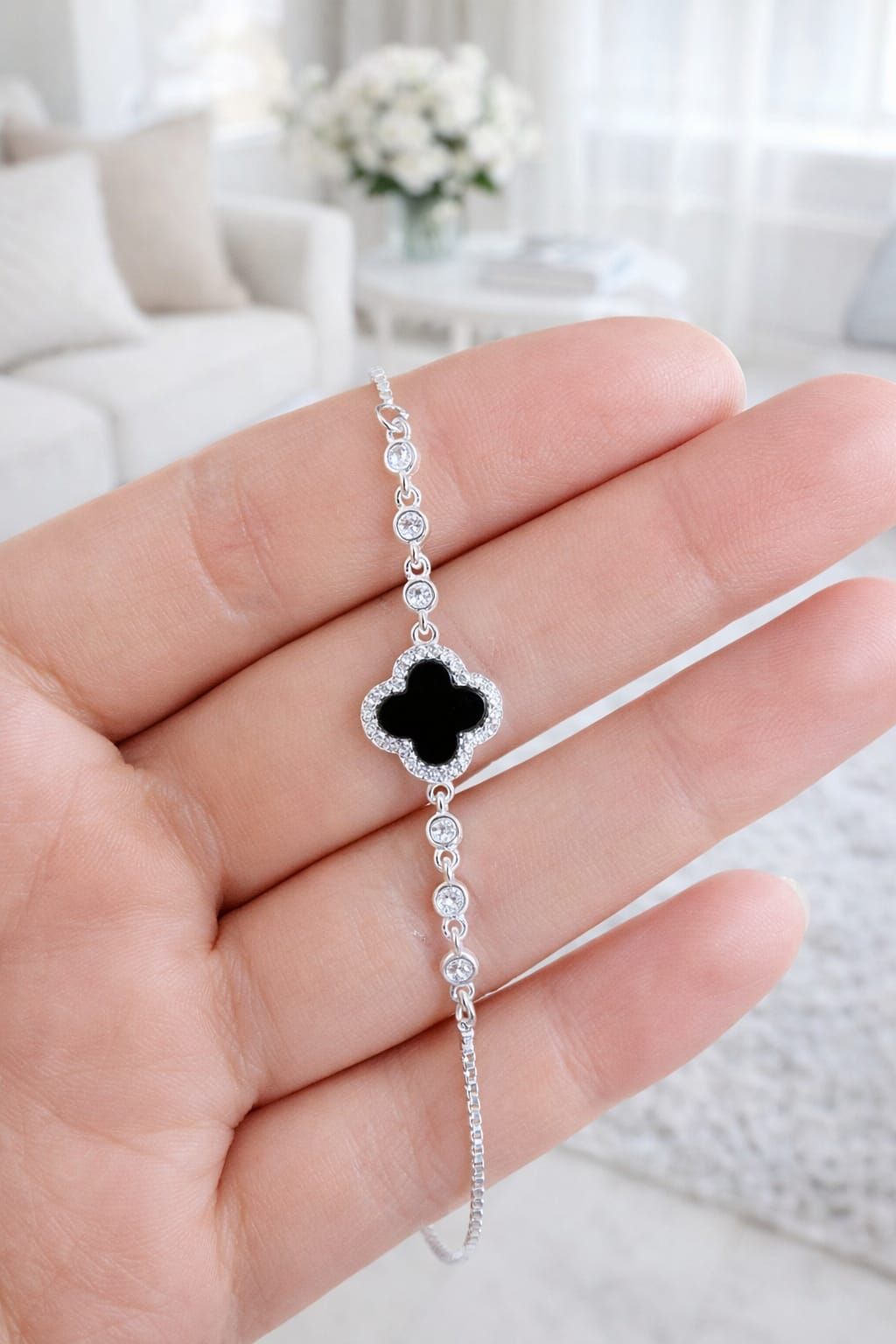 Pulsera de plata con un dije de trébol negro en la muñeca