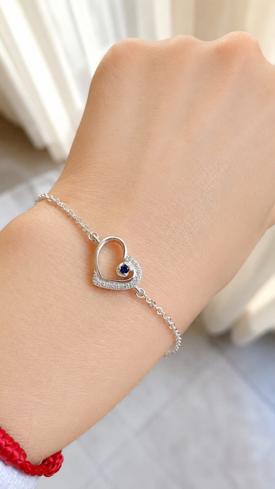 Primer plano de una muñeca con una pulsera plateada en forma de corazón con una piedra azul oscuro en el centro.