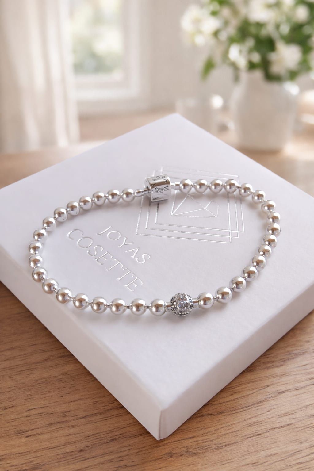 Pulsera de cuentas de plata en la muñeca con un pequeño cierre rectangular.