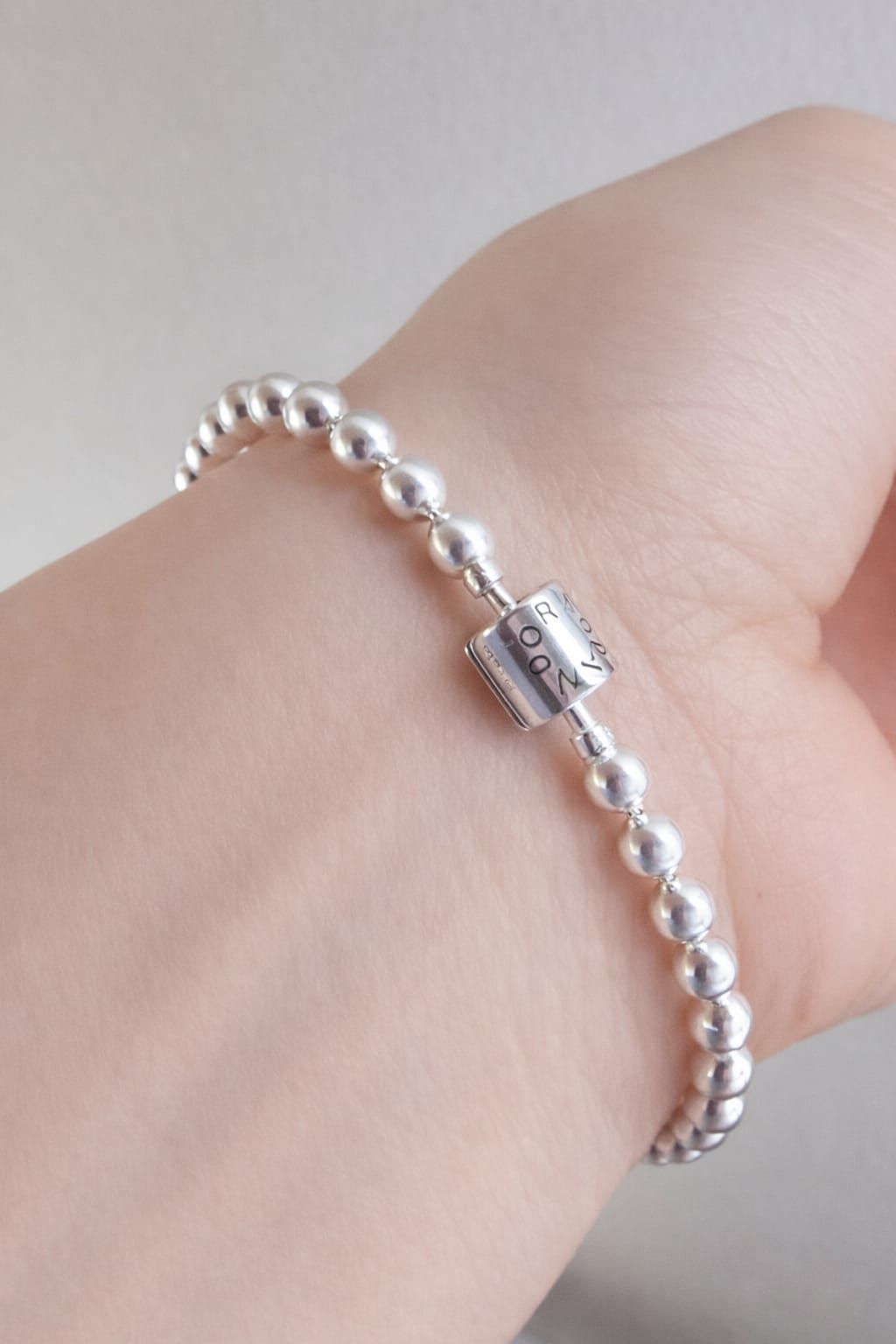 Pulsera de cuentas de plata en la muñeca con un pequeño cierre rectangular.