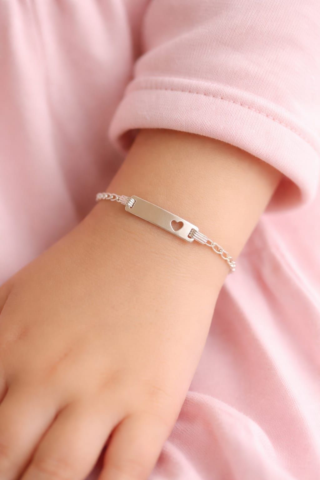 Pulsera plateada en la muñeca sobre una manga rosa.