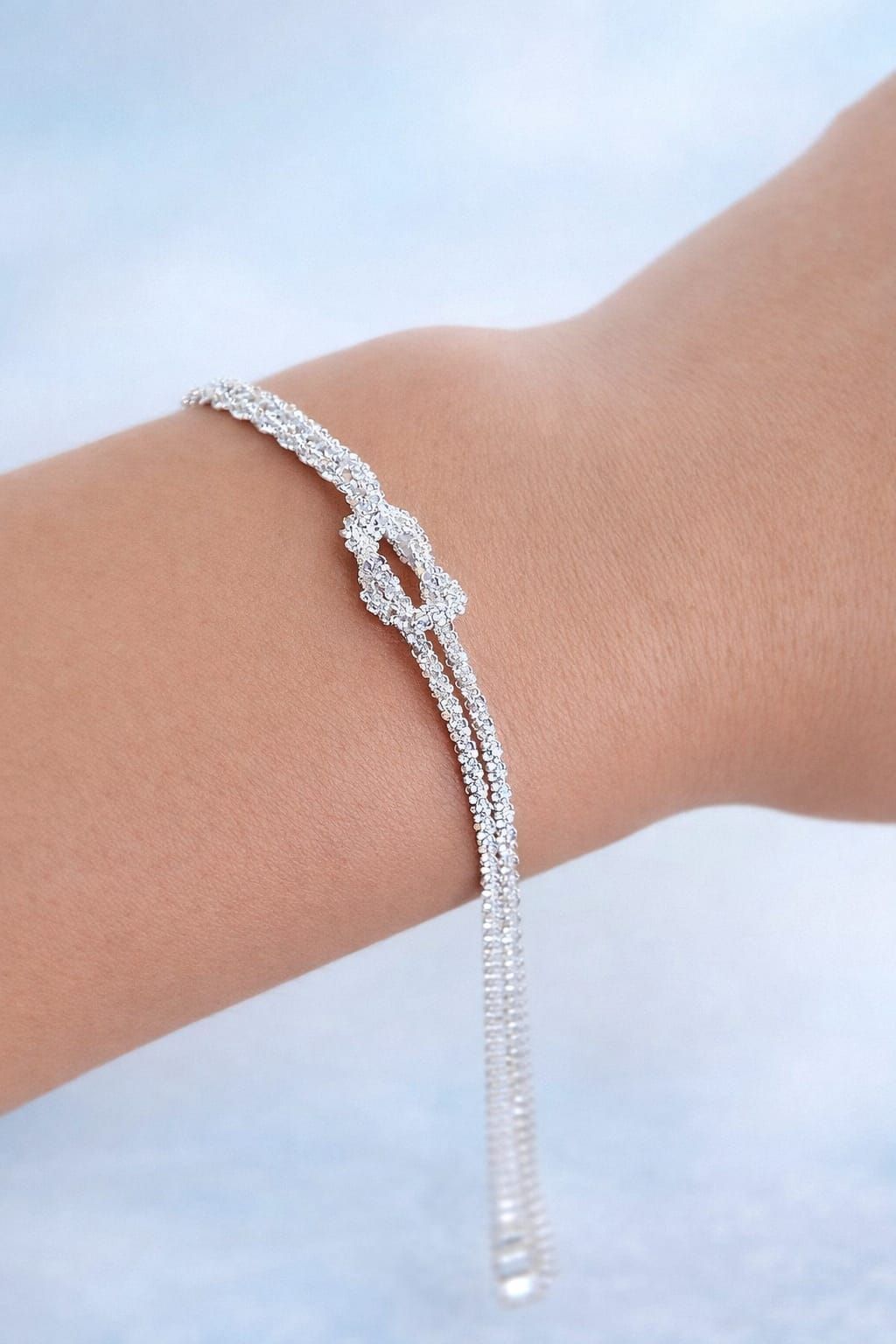 Pulsera de plata con una cadena colgante en una muñeca sobre un fondo claro.