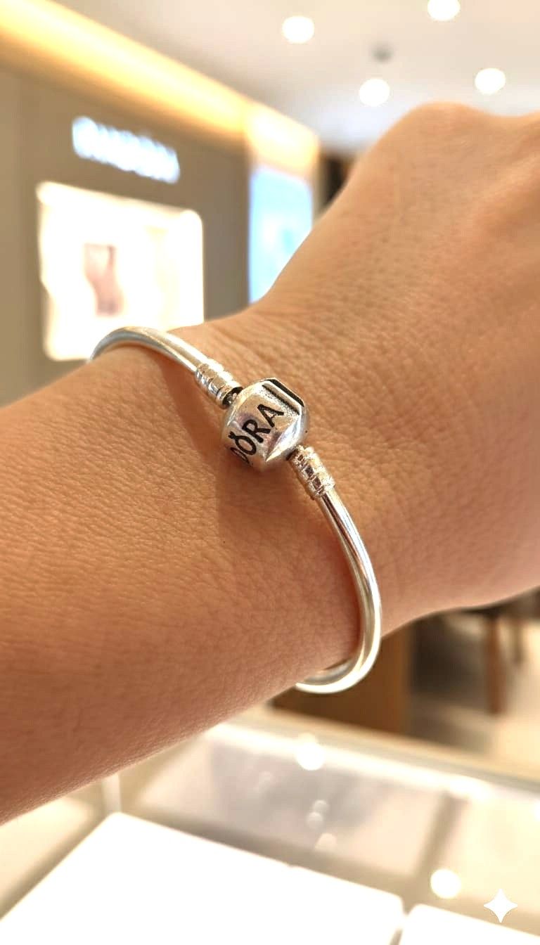 Primer plano de una pulsera de plata con dijes en la muñeca, en una tienda con iluminación tenue.