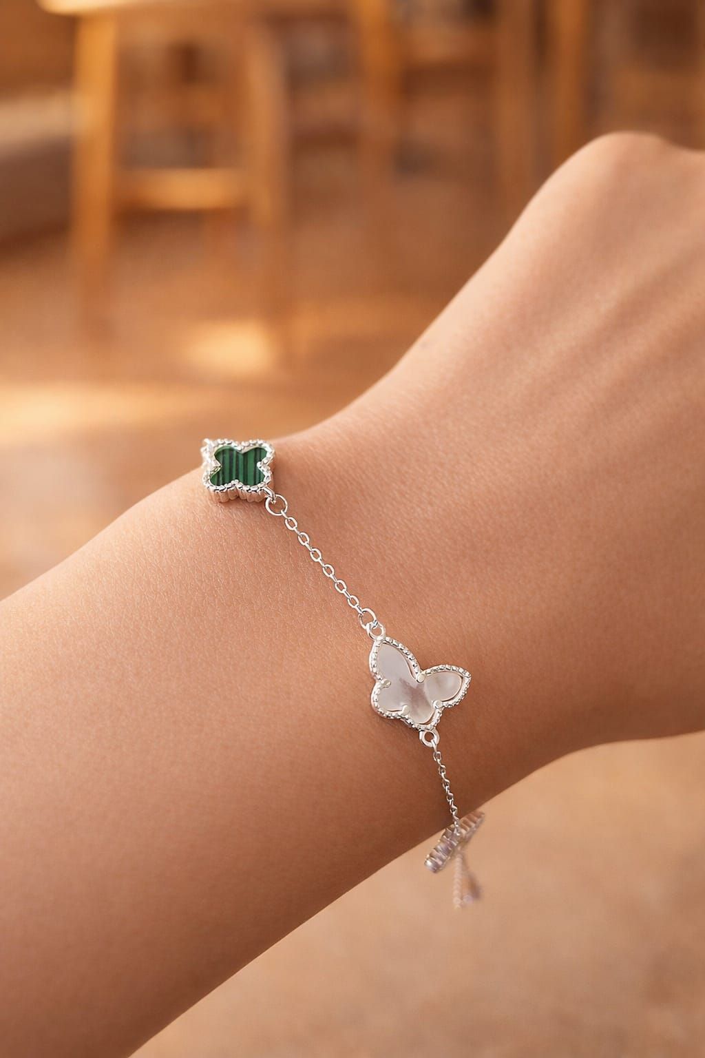 Primer plano de una muñeca que luce una pulsera de mariposa plateada con un dije de trébol verde.