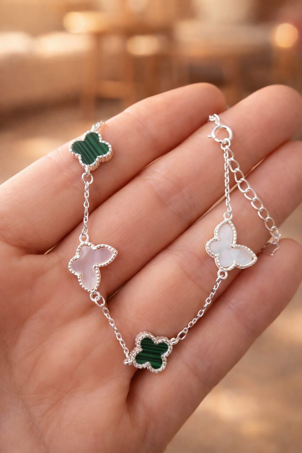 Primer plano de una muñeca que luce una pulsera de mariposa plateada con un dije de trébol verde.
