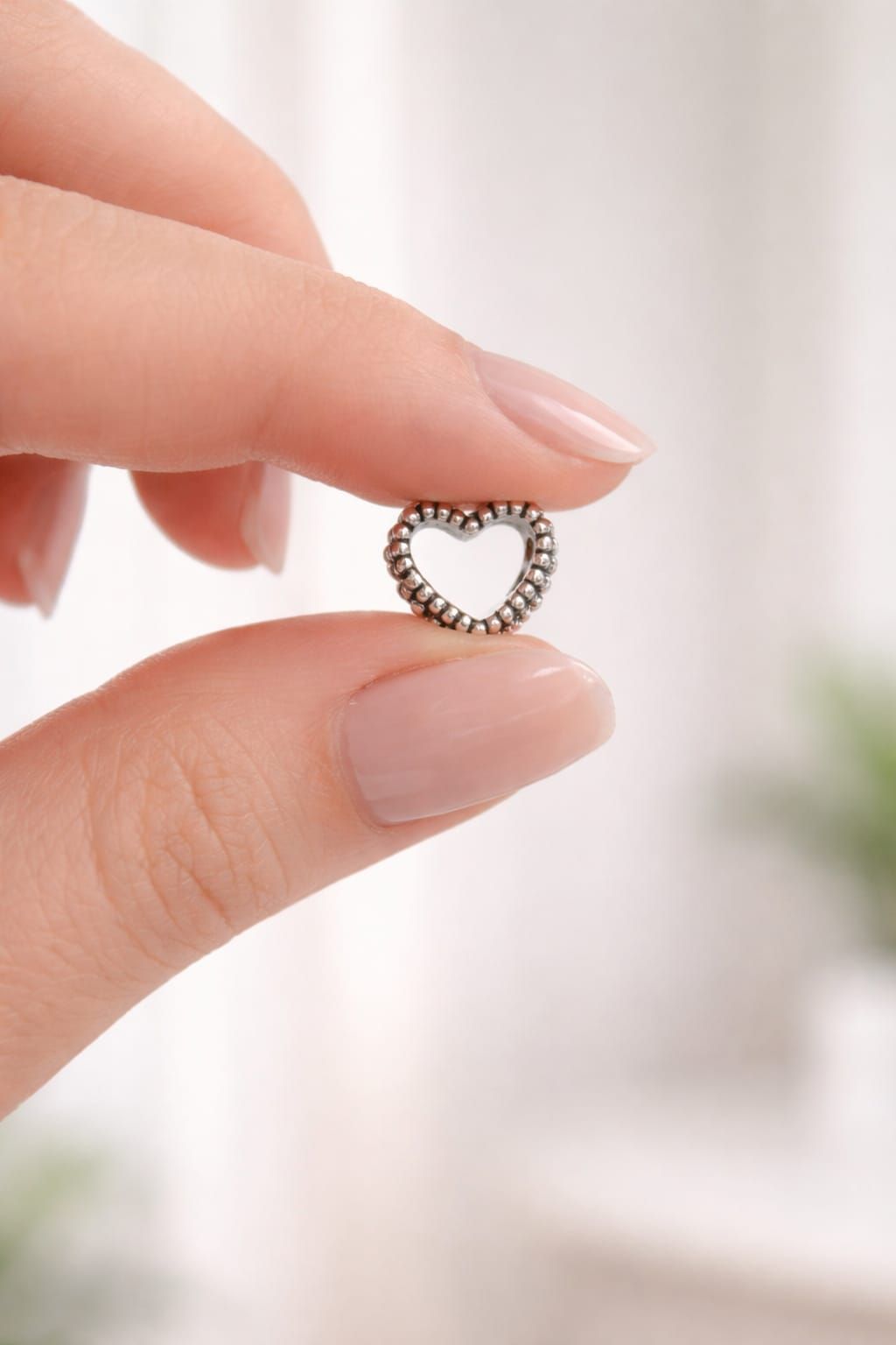 Mano sosteniendo un pequeño anillo de cuentas en forma de corazón sobre un fondo suave y desenfocado.