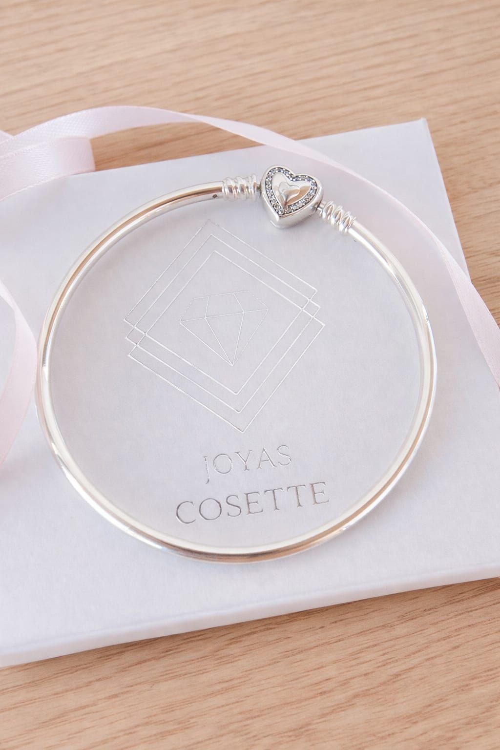 Pulsera con dije de corazón plateado en una muñeca sobre un fondo claro.