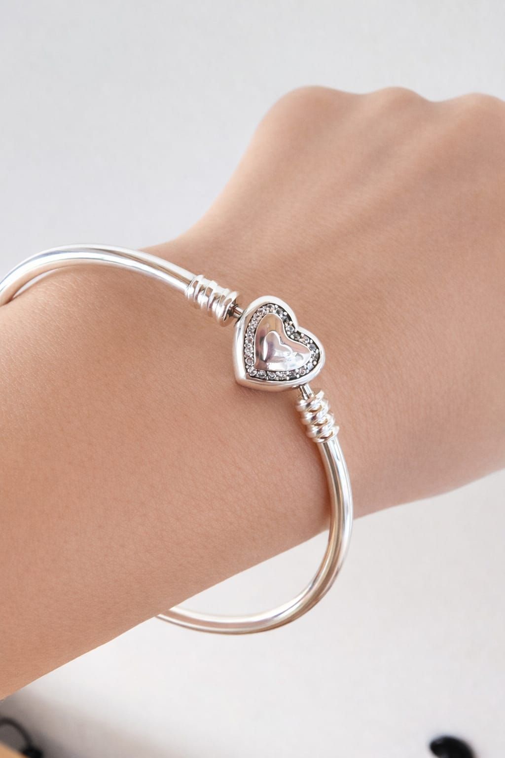 Pulsera con dije de corazón plateado en una muñeca sobre un fondo claro.