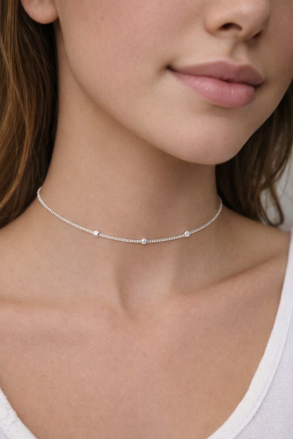 Primer plano de una mujer que lleva un delicado collar de plata con pequeños detalles de cuentas y una blusa blanca.