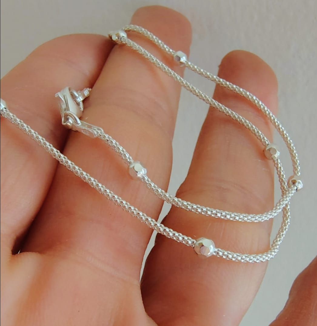Primer plano de una mujer que lleva un delicado collar de plata con pequeños detalles de cuentas y una blusa blanca.