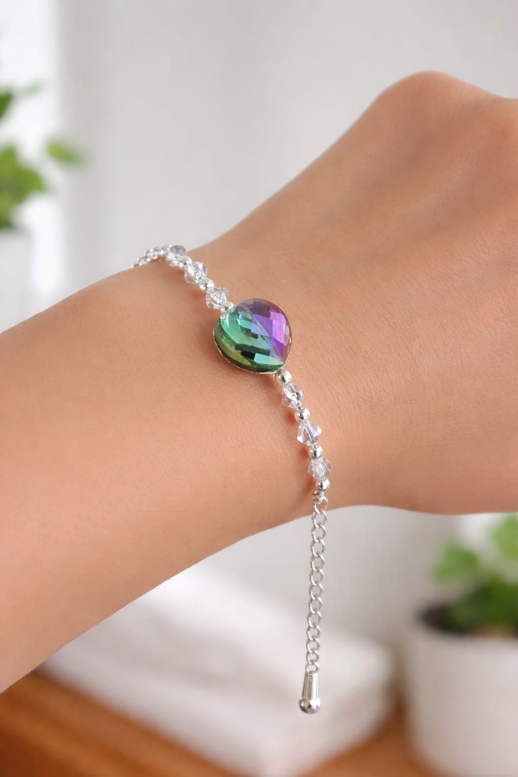 Mano con una pulsera de plata con un dije de piedra preciosa verde-morada, colgando sobre un fondo interior borroso.