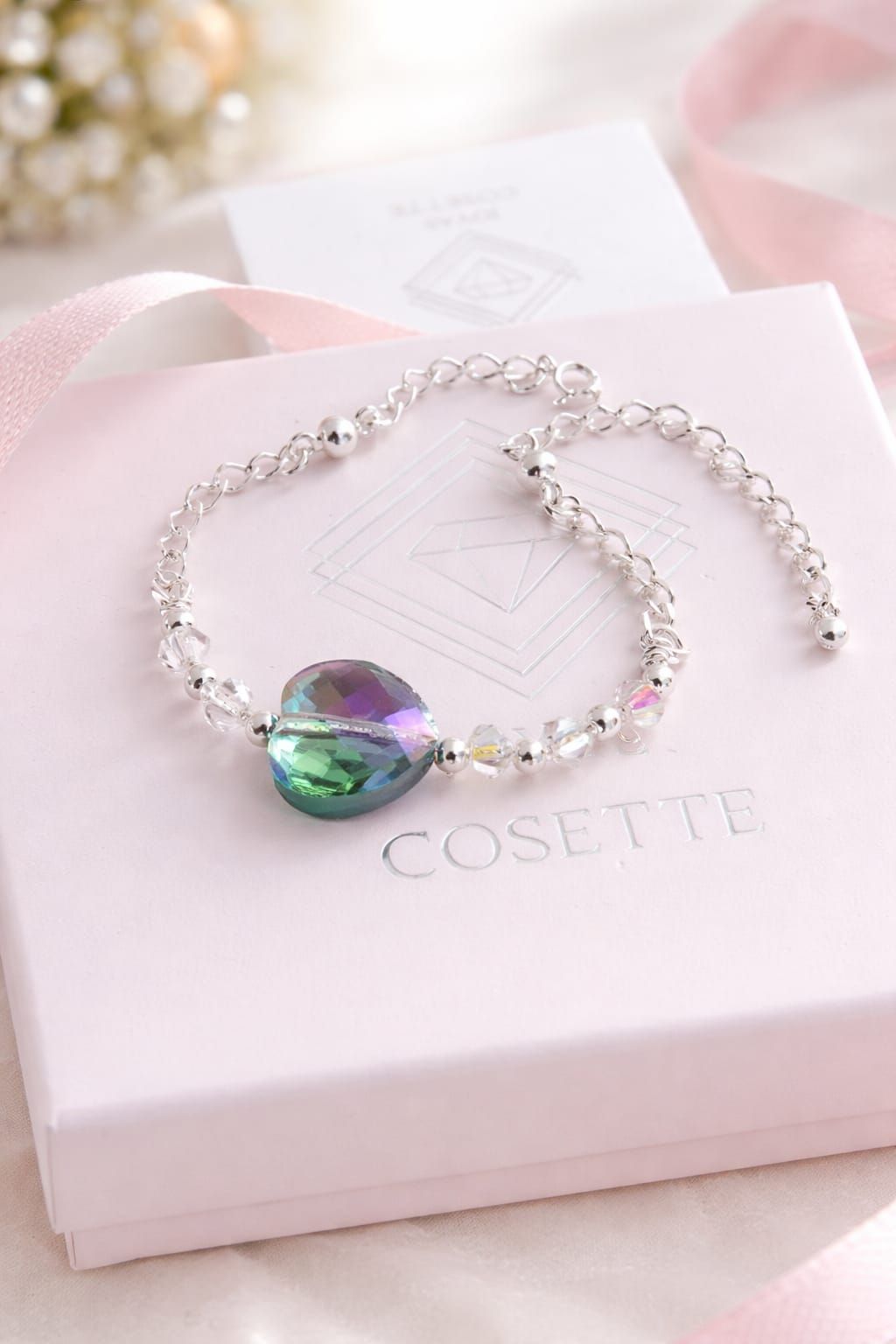 Mano con una pulsera de plata con un dije de piedra preciosa verde-morada, colgando sobre un fondo interior borroso.