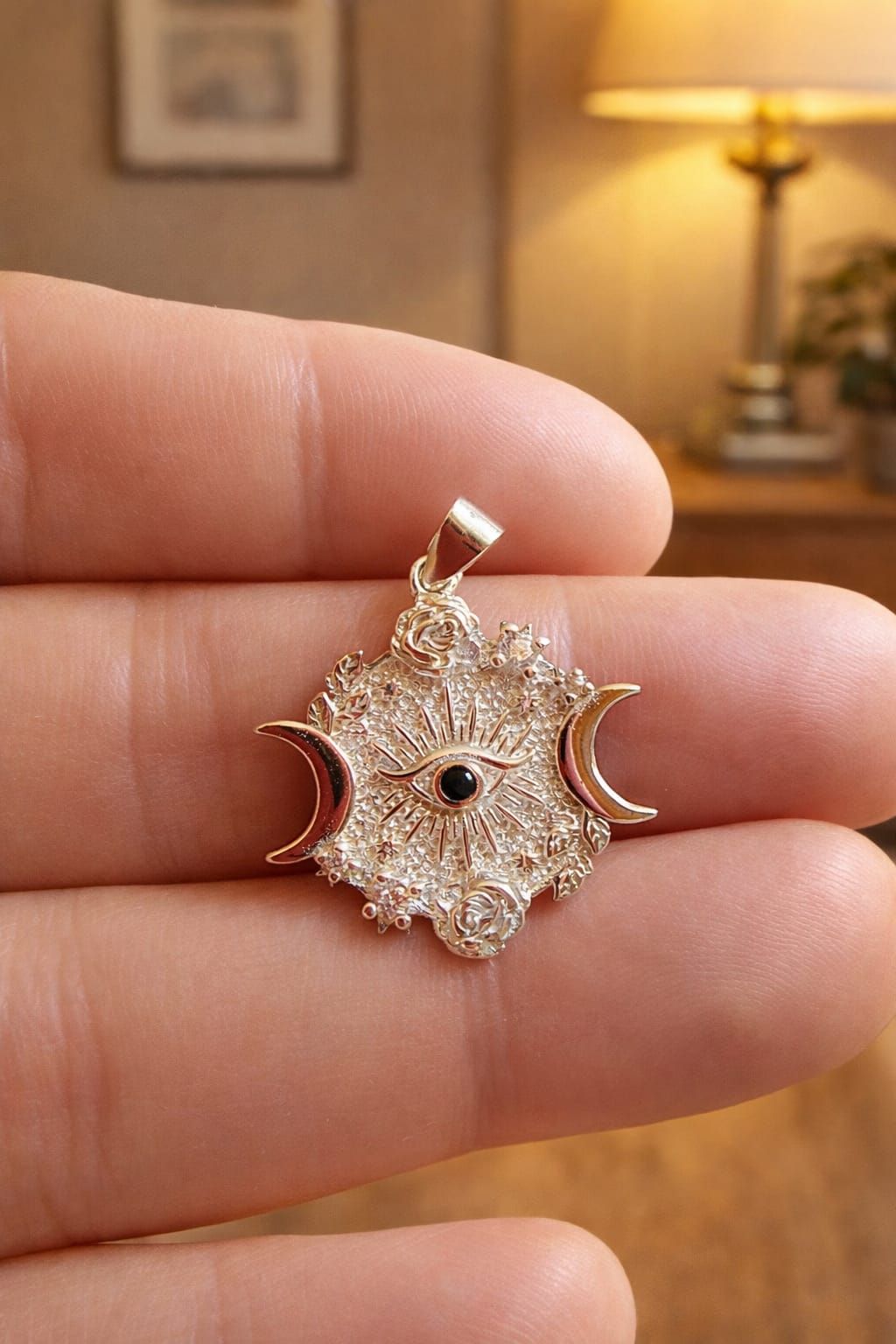 Primer plano de un pequeño colgante de oro con forma de sol y luna sostenido entre los dedos, con una habitación tenuemente