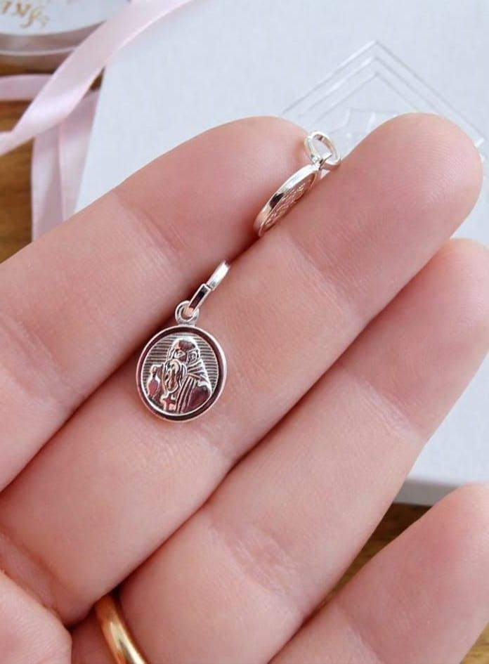 Colgante de plata con forma de santo en una mano, con un medallón circular grabado y un broche.