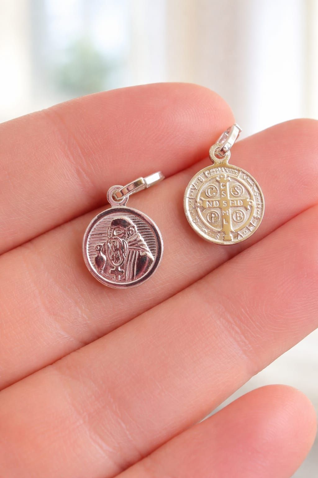 Colgante de plata con forma de santo en una mano, con un medallón circular grabado y un broche.