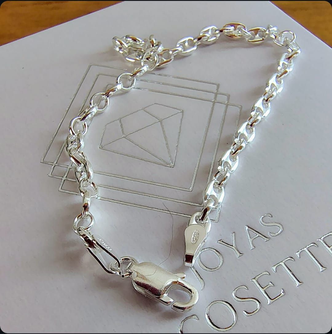 Pulsera de cadena plateada en una caja de joyería blanca con logotipo geométrico en relieve y texto.