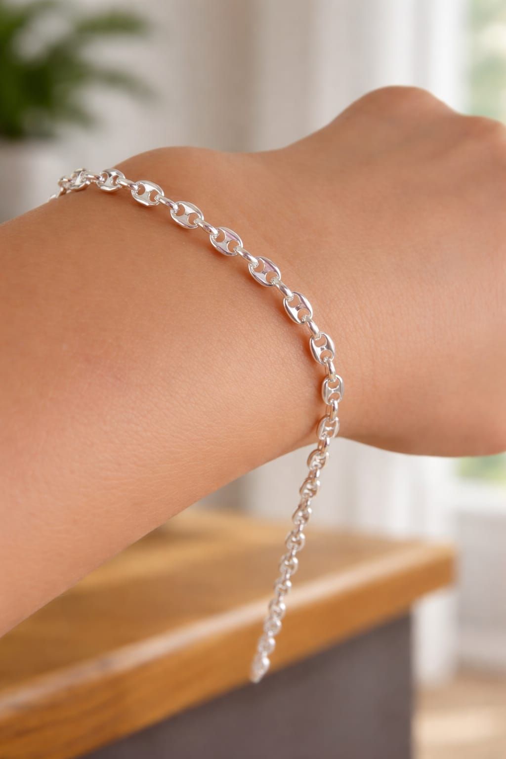 Pulsera de cadena plateada en una caja de joyería blanca con logotipo geométrico en relieve y texto.