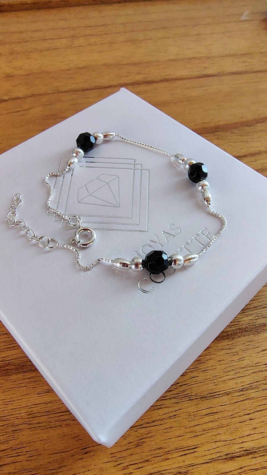 Pulsera plateada con cuentas negras en una muñeca, vista de cerca.