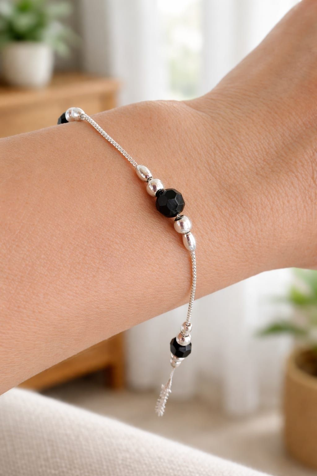 Pulsera plateada con cuentas negras en una muñeca, vista de cerca.