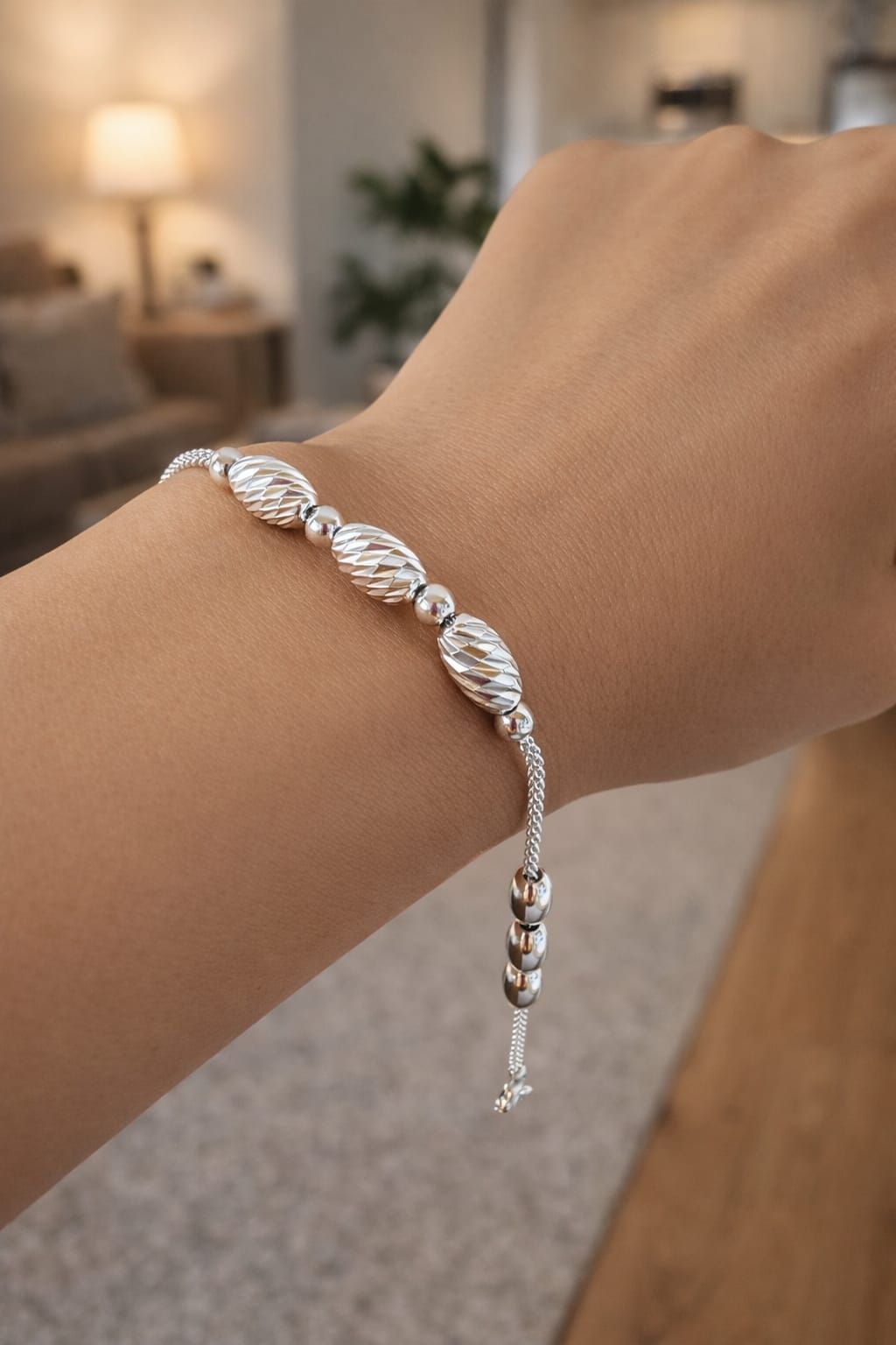 Pulsera de cuentas plateadas sobre una mano, con un anillo dorado en primer plano y un fondo de habitación suavemente