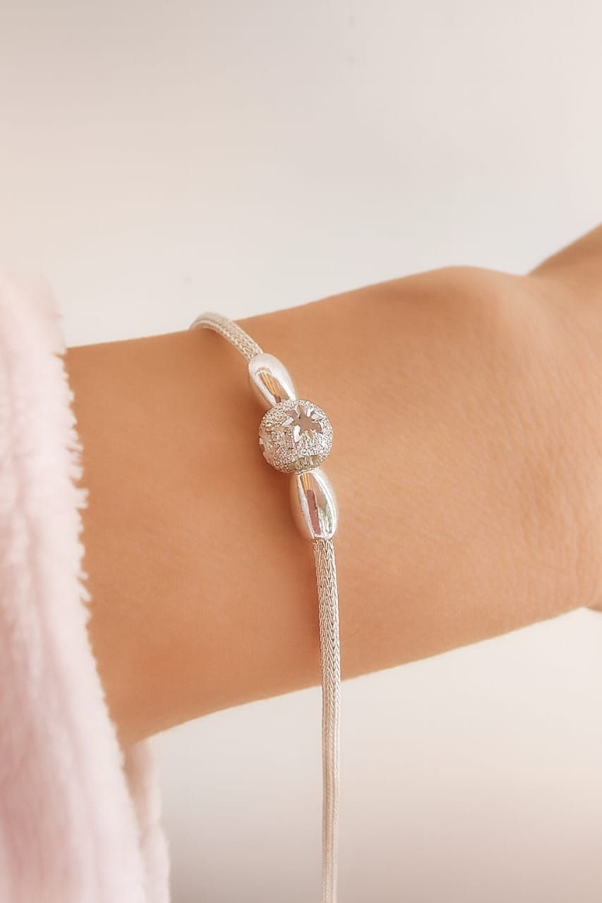Pulsera de plata con un centro floral redondo en la muñeca sobre un fondo blanco suave.