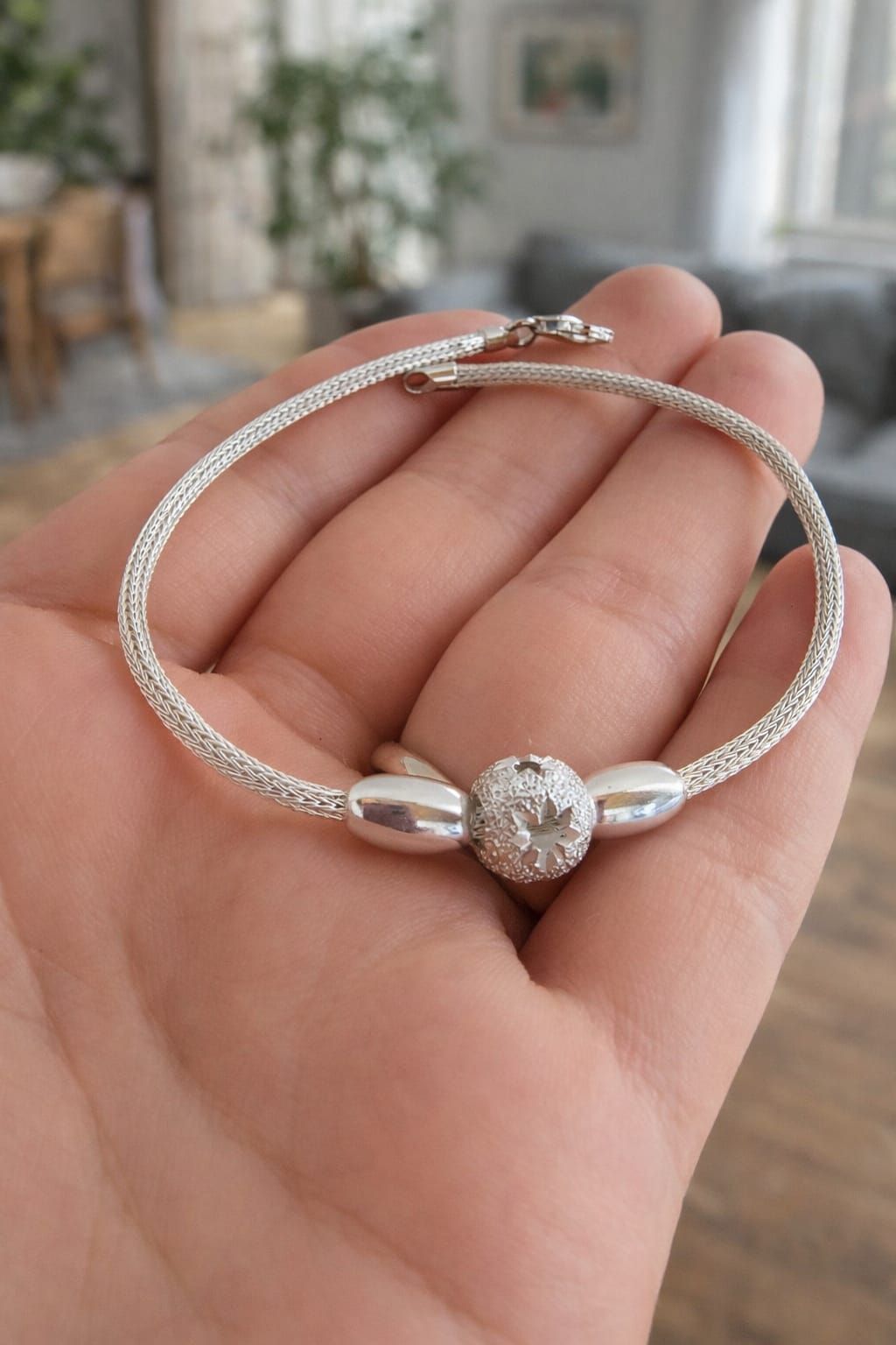 Pulsera de plata con un centro floral redondo en la muñeca sobre un fondo blanco suave.