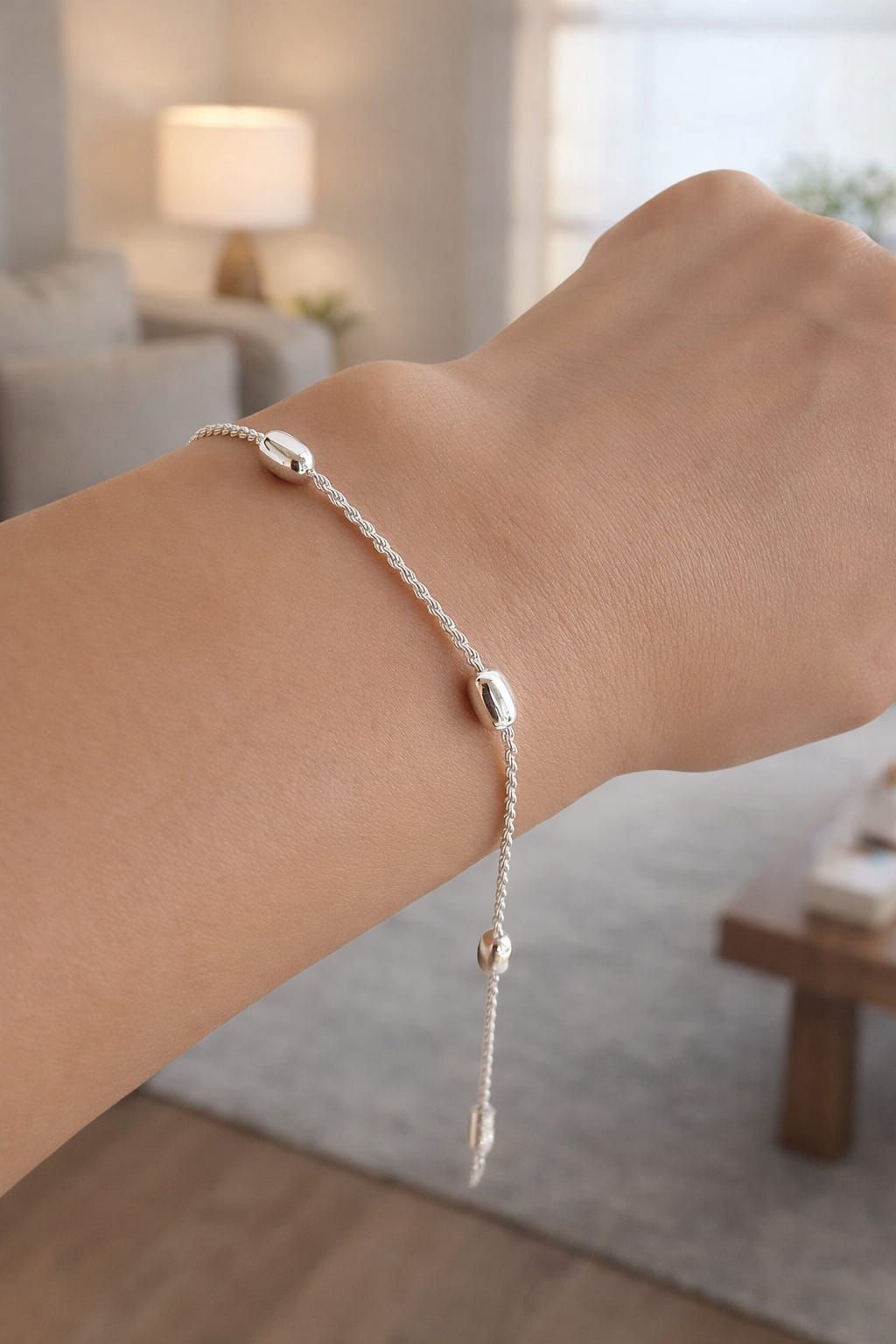 Pulsera de plata con cadena colgante en una muñeca en una habitación con iluminación tenue.