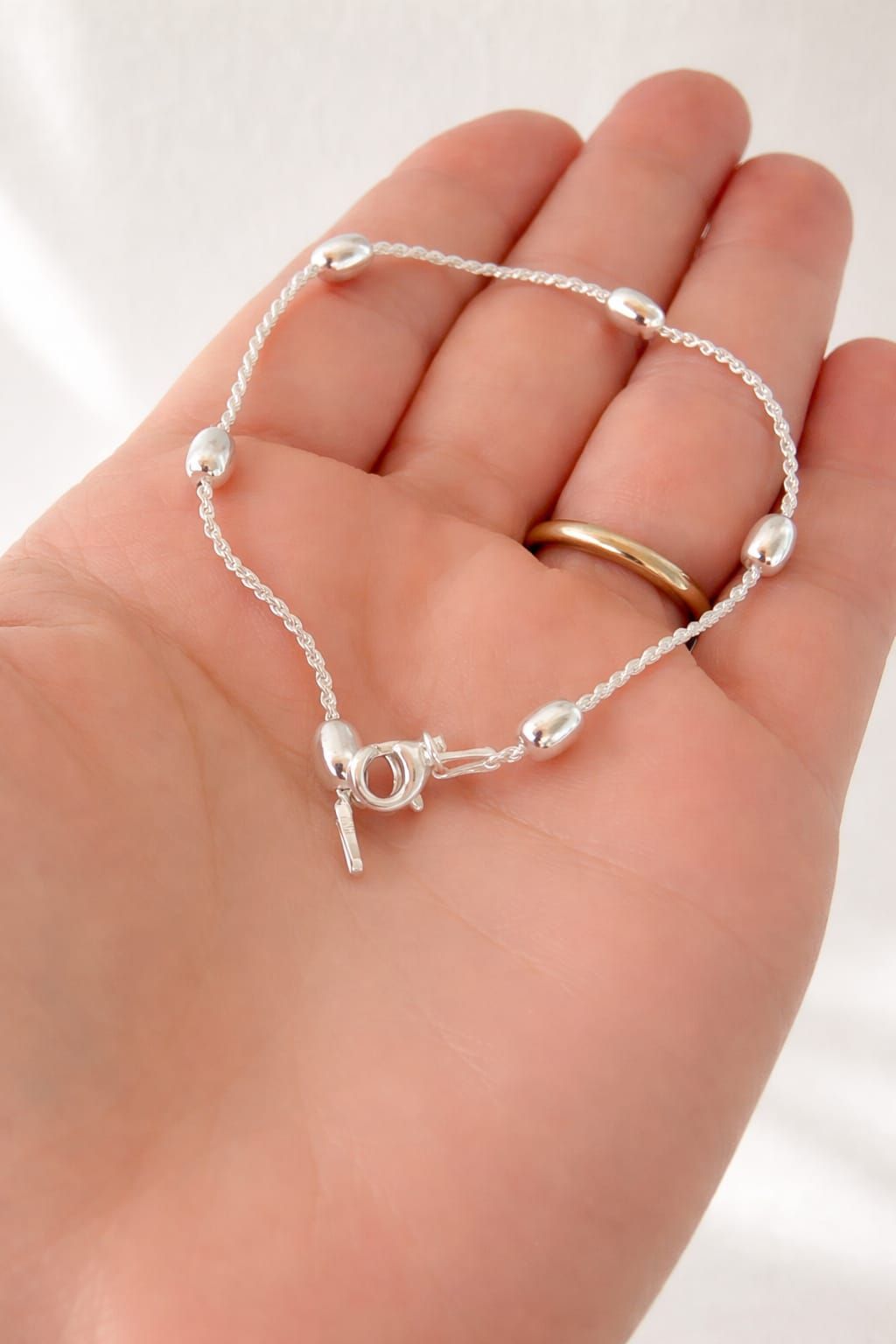 Pulsera de plata con cadena colgante en una muñeca en una habitación con iluminación tenue.