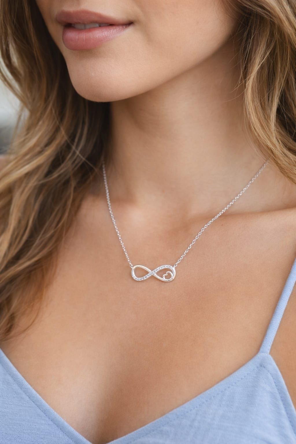 Mujer con un collar de infinito plateado sobre una blusa azul claro.
