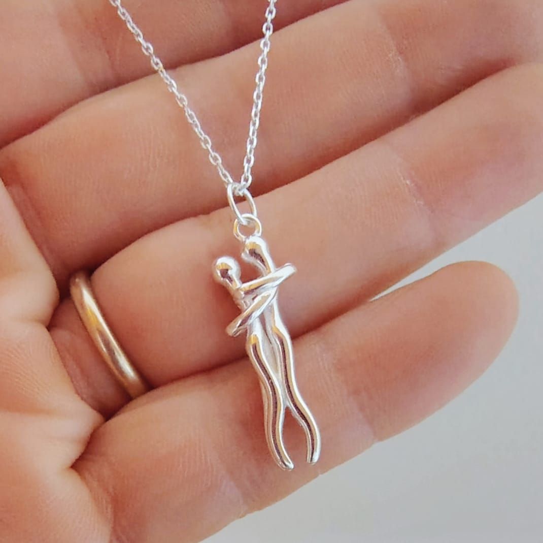 Collar de plata con un pequeño colgante en el cuello de una mujer sobre una blusa blanca con escote en V.