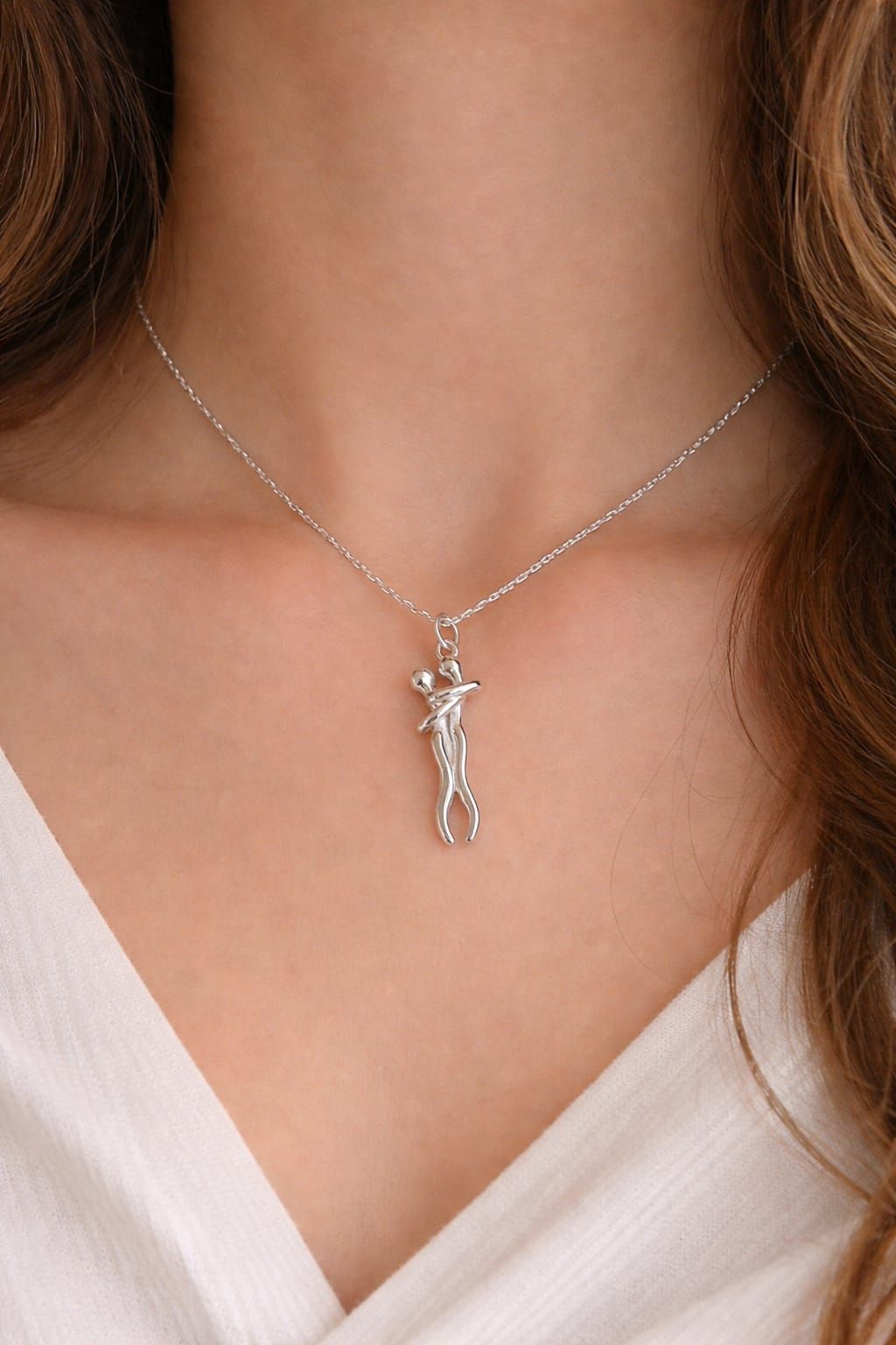 Collar de plata con un pequeño colgante en el cuello de una mujer sobre una blusa blanca con escote en V.