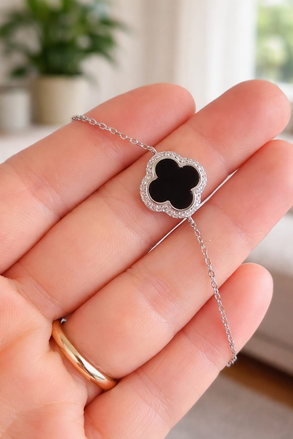 Collar con colgante de trébol plateado con centro negro, que descansa sobre una mano.