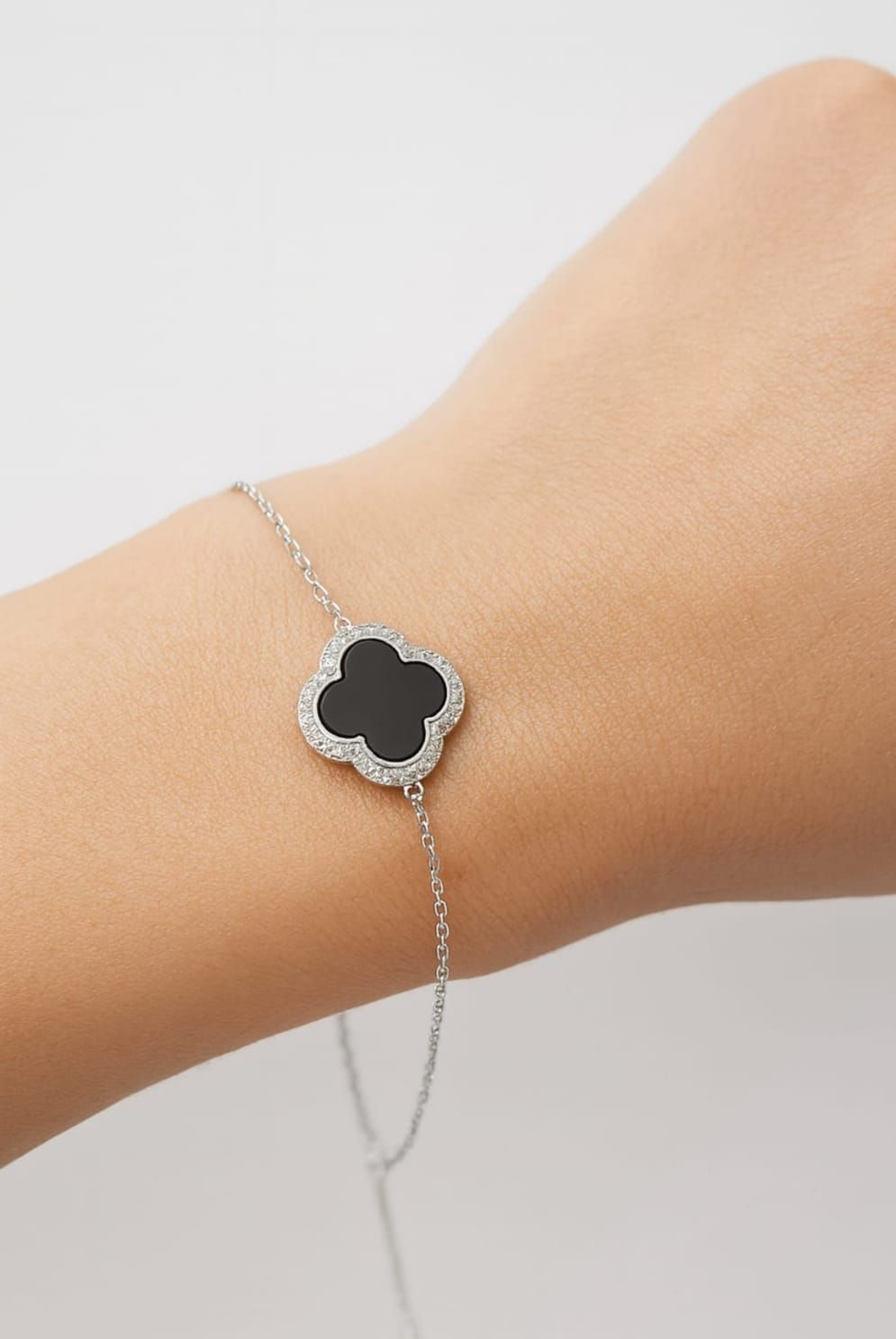 Collar con colgante de trébol plateado con centro negro, que descansa sobre una mano.