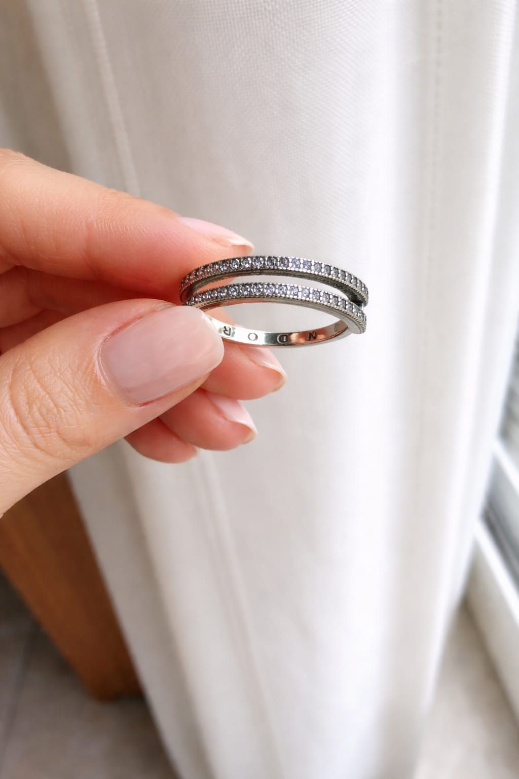 Mano con manicura rosa y anillos de plata cerca de una ventana y balcón con vistas