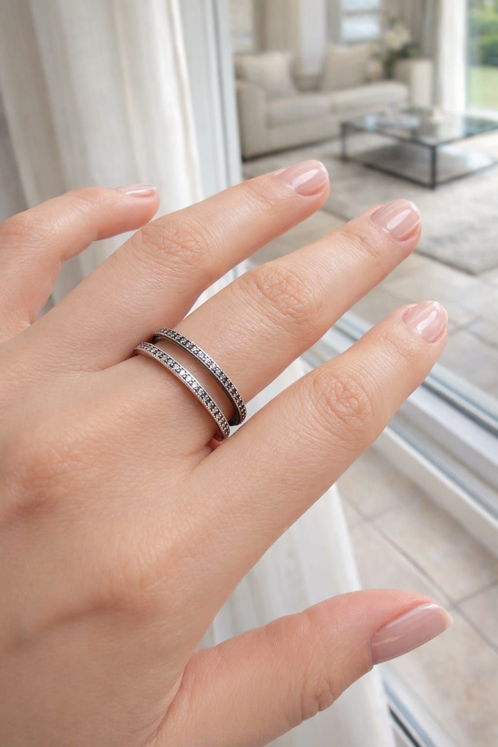 Mano con manicura rosa y anillos de plata cerca de una ventana y balcón con vistas