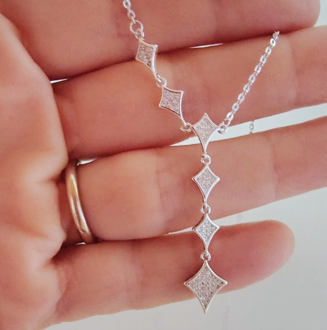 Mujer con un collar plateado en forma de Y con dijes de diamantes y una blusa blanca.