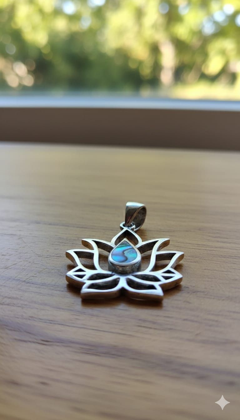 Pequeño colgante de plata con forma de loto y una gema verde en forma de lágrima, sostenido entre los dedos.