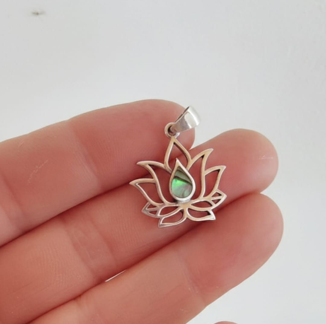 Pequeño colgante de plata con forma de loto y una gema verde en forma de lágrima, sostenido entre los dedos.