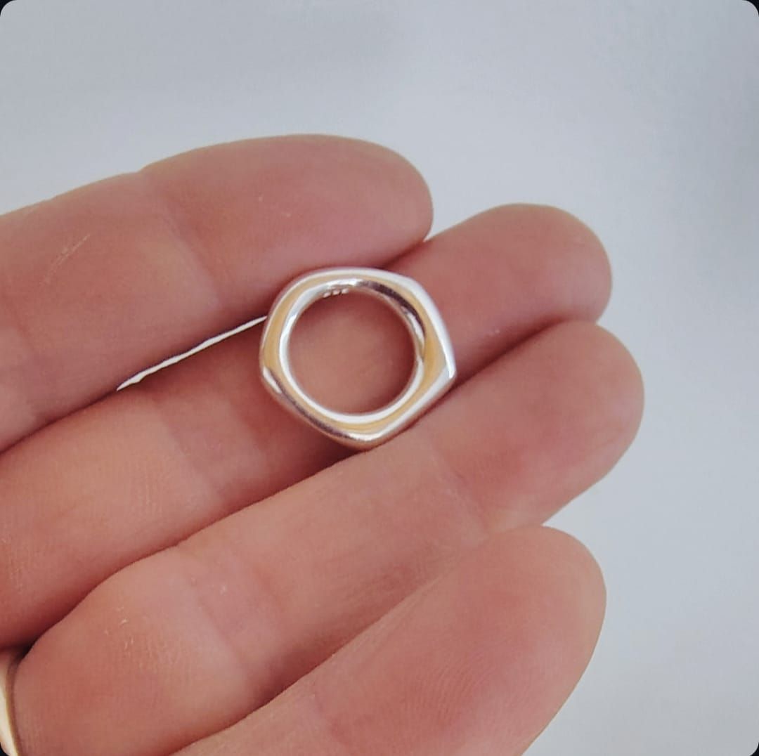 Primer plano de collares dorados superpuestos con un colgante circular sobre una blusa gris con escote en V.