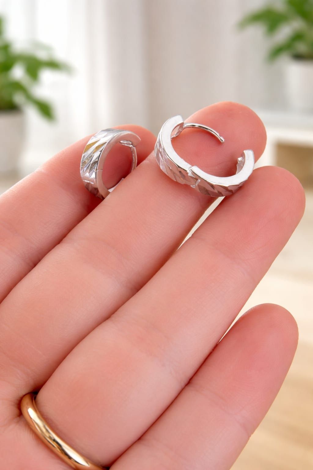 Mano sosteniendo un anillo de plata con una piedra transparente sobre un fondo suave y brillante.