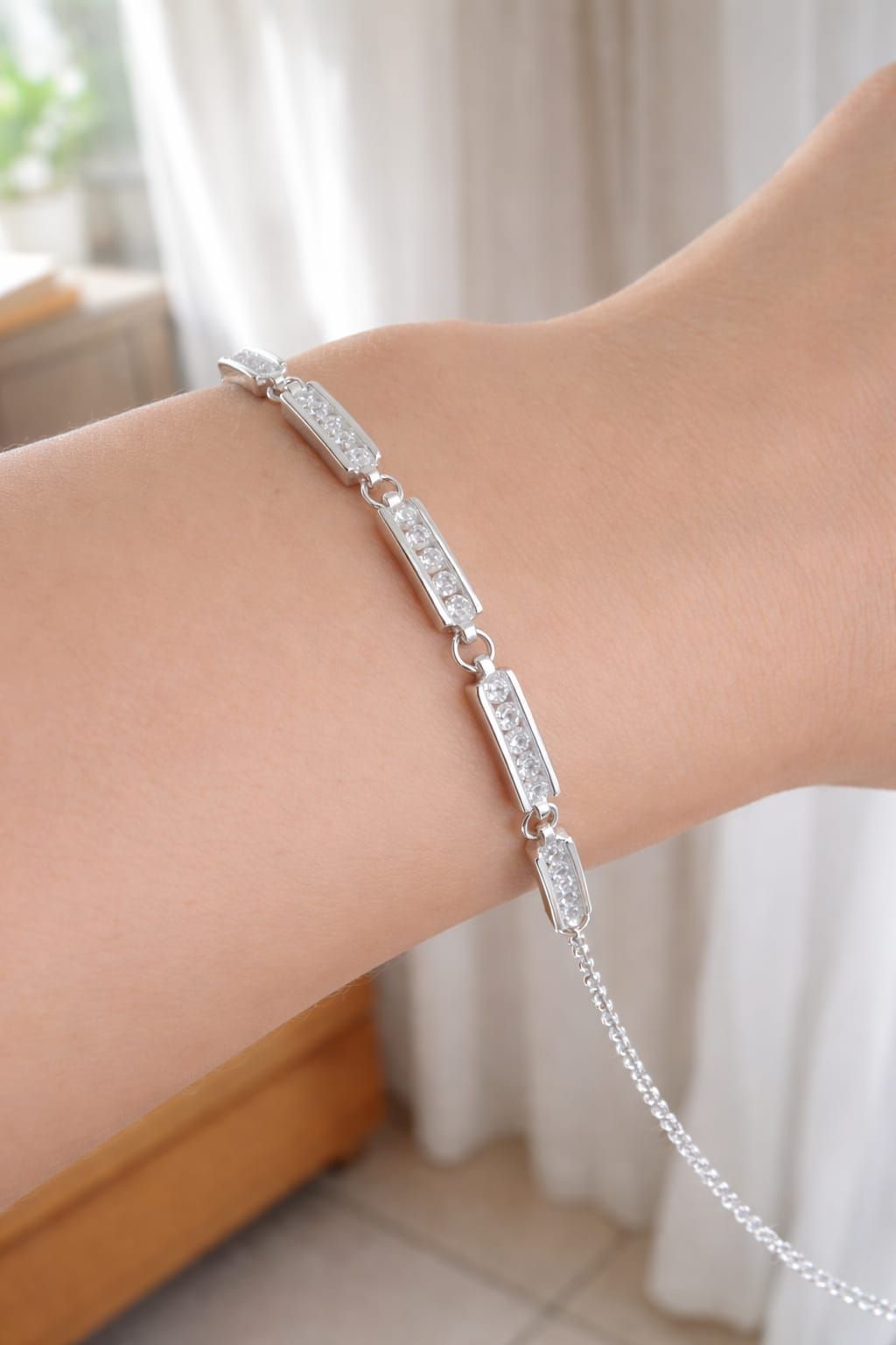 Pulsera de plata con piedras rectangulares en una muñeca, fotografiada en interiores cerca de una cortina.