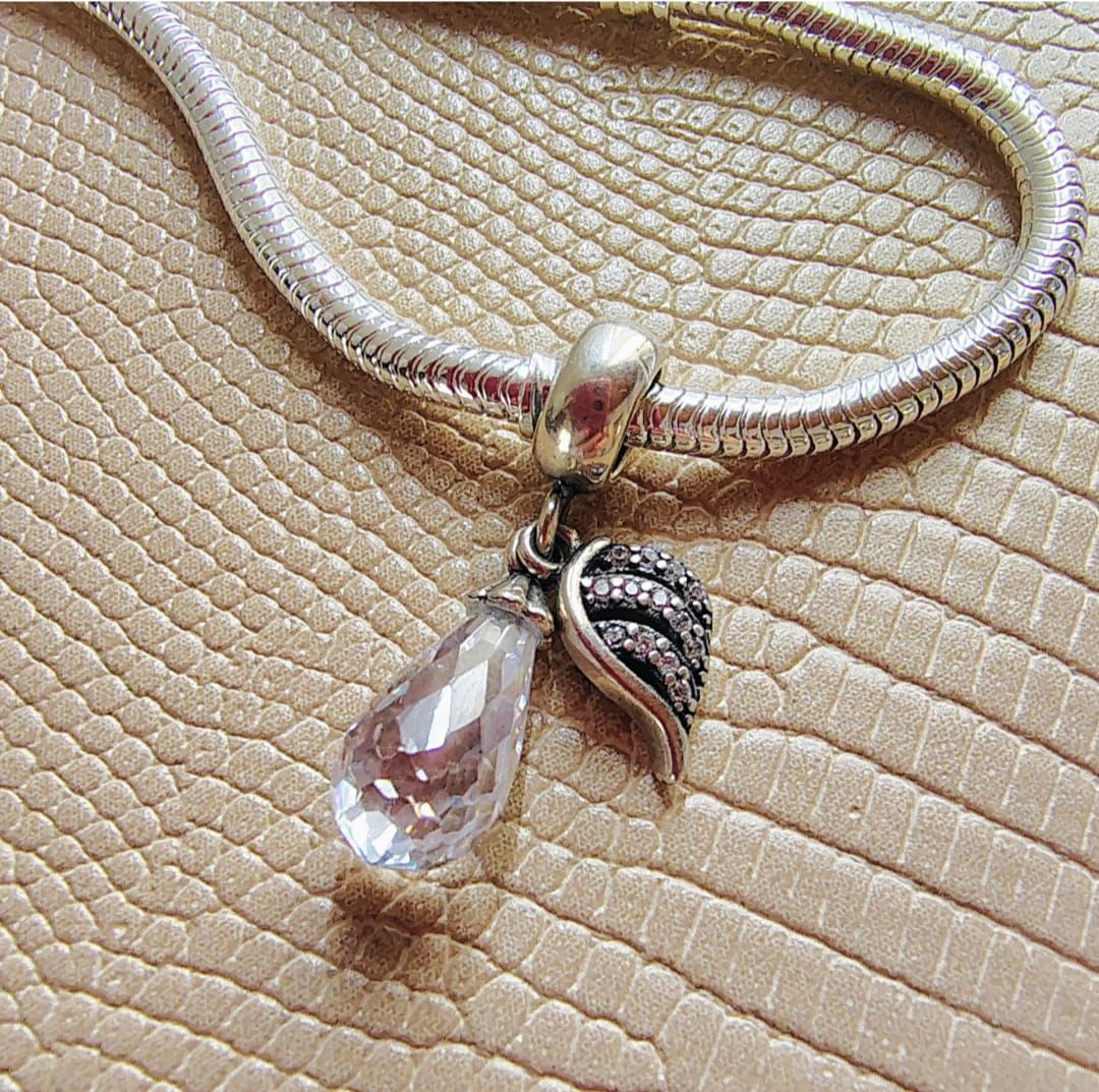 Una mano sostiene un pequeño colgante de flor de cristal y oro rosa en una sala de estar iluminada por el sol.